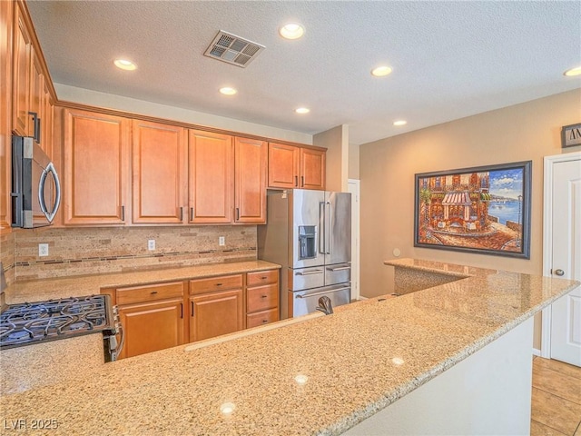 kitchen with visible vents, backsplash, appliances with stainless steel finishes, light stone countertops, and a peninsula