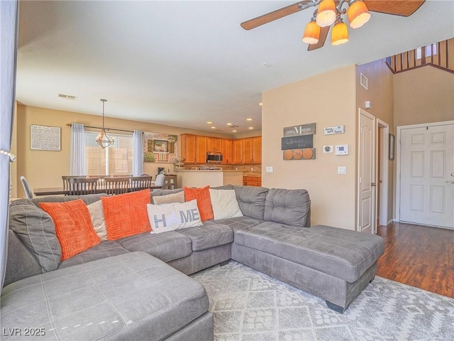 living room with ceiling fan with notable chandelier, visible vents, and wood finished floors