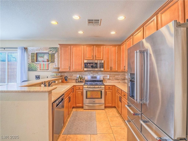 kitchen featuring light tile patterned floors, a peninsula, a sink, stainless steel appliances, and backsplash