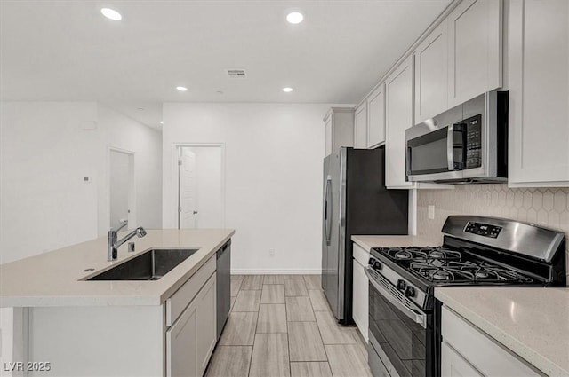 kitchen with visible vents, an island with sink, a sink, stainless steel appliances, and backsplash