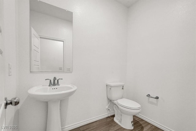 half bathroom featuring toilet, baseboards, and wood finished floors