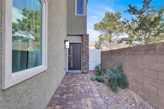 view of exterior entry with fence and stucco siding