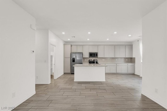 kitchen featuring a center island, wood finish floors, stainless steel appliances, tasteful backsplash, and light countertops