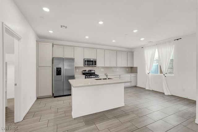 kitchen with a kitchen island with sink, visible vents, light countertops, appliances with stainless steel finishes, and backsplash