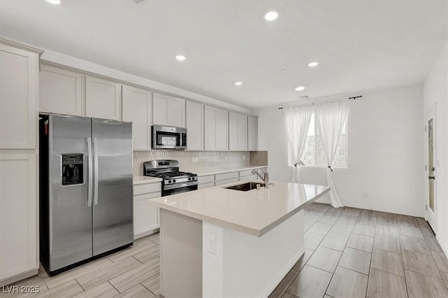 kitchen with stainless steel appliances, light countertops, backsplash, a kitchen island with sink, and a sink