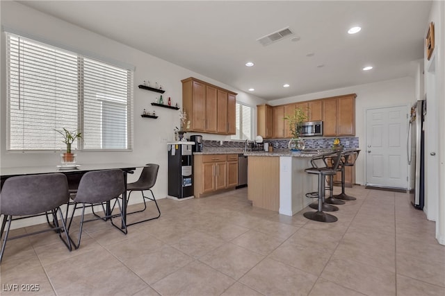 kitchen featuring a breakfast bar, a kitchen island, visible vents, appliances with stainless steel finishes, and brown cabinets