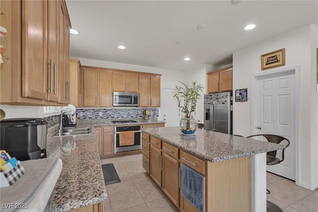 kitchen with light stone countertops, a kitchen island, stainless steel appliances, and a sink