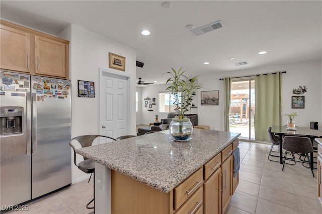 kitchen with light stone counters, stainless steel refrigerator with ice dispenser, a kitchen island, and visible vents