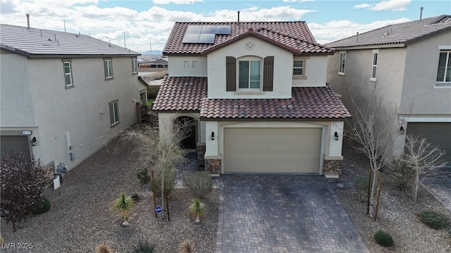 mediterranean / spanish-style house with stucco siding, decorative driveway, a tile roof, and solar panels