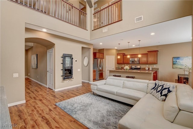 living area featuring light wood-type flooring, visible vents, arched walkways, and baseboards