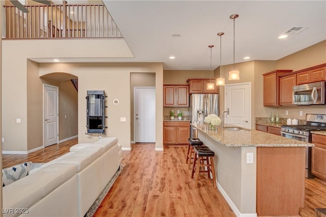 kitchen featuring visible vents, a sink, open floor plan, stainless steel appliances, and light wood finished floors