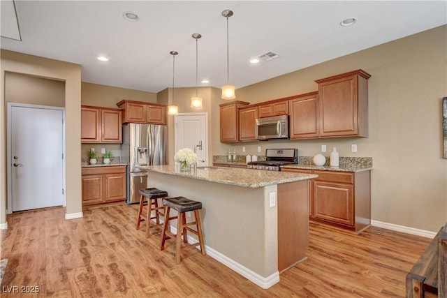 kitchen with a breakfast bar, an island with sink, light wood-style flooring, appliances with stainless steel finishes, and brown cabinetry