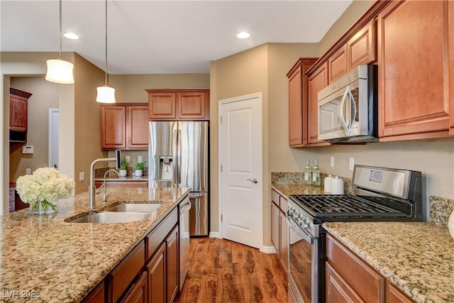 kitchen featuring pendant lighting, light stone counters, wood finished floors, stainless steel appliances, and a sink