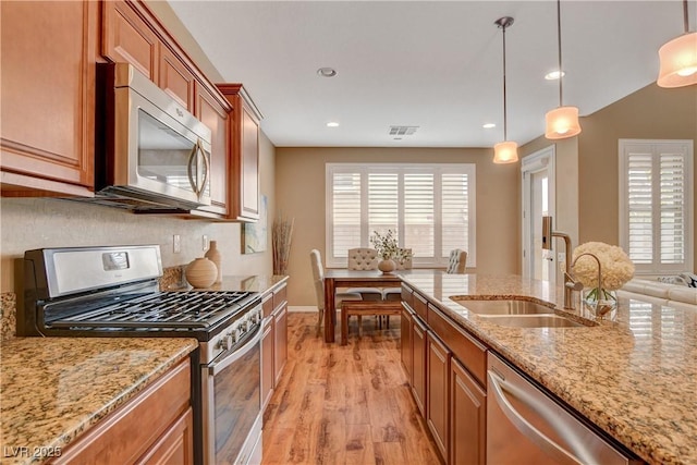 kitchen with a sink, appliances with stainless steel finishes, brown cabinetry, and light wood finished floors