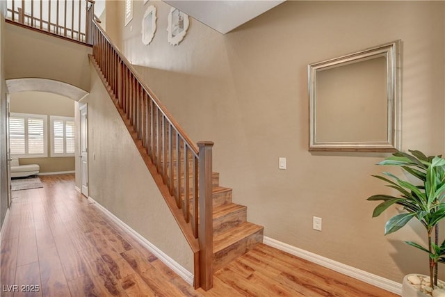 stairs featuring a high ceiling, wood finished floors, baseboards, and arched walkways