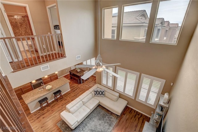 living room with a ceiling fan, wood finished floors, visible vents, and a towering ceiling