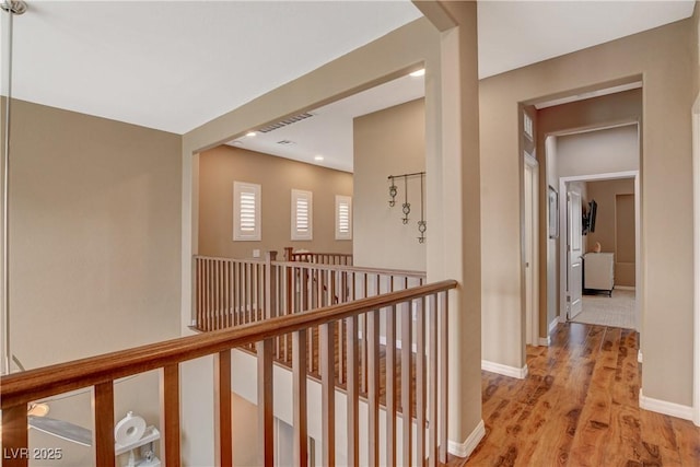 hall with baseboards, an upstairs landing, visible vents, and light wood finished floors