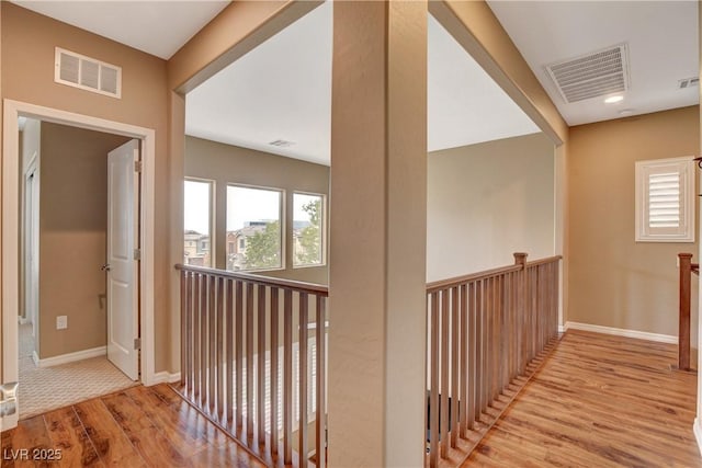 hall with an upstairs landing, wood finished floors, visible vents, and baseboards