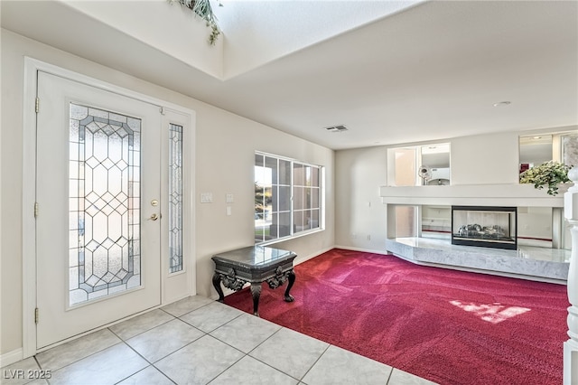 entryway featuring visible vents, a high end fireplace, carpet flooring, and tile patterned flooring