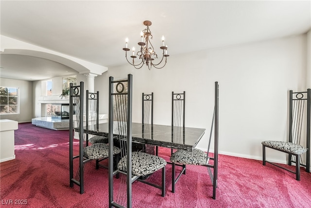 carpeted dining space featuring decorative columns, arched walkways, a notable chandelier, and baseboards