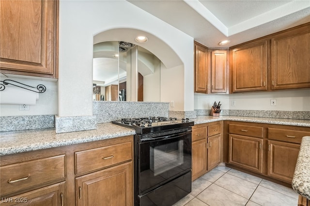 kitchen featuring black gas range, light tile patterned flooring, and brown cabinetry