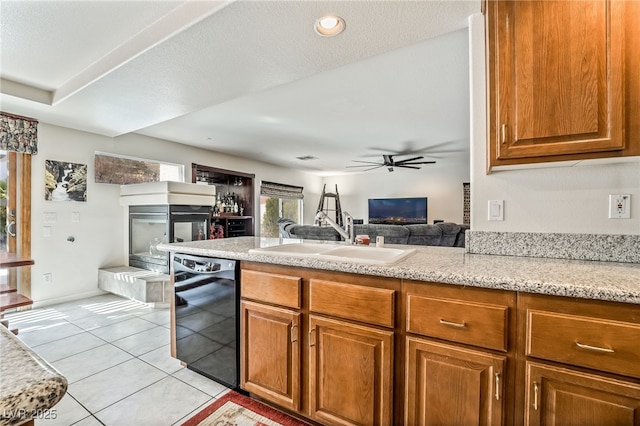 kitchen with a multi sided fireplace, dishwasher, light tile patterned floors, a ceiling fan, and a sink