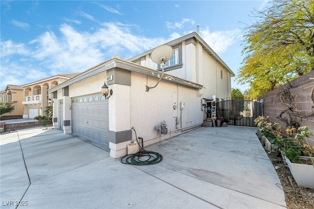 view of side of property featuring a gate, fence, driveway, an attached garage, and stucco siding