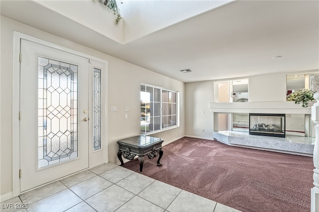 carpeted entryway featuring a premium fireplace, baseboards, visible vents, and tile patterned floors