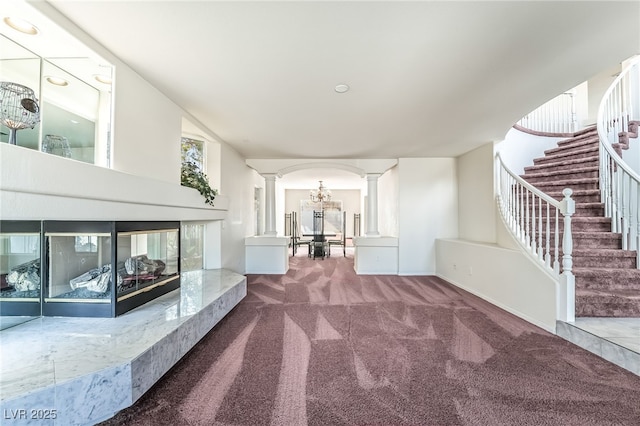 unfurnished living room featuring stairway, carpet, and ornate columns