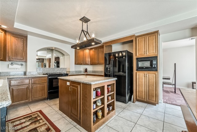 kitchen featuring a center island, brown cabinetry, black appliances, arched walkways, and light stone countertops