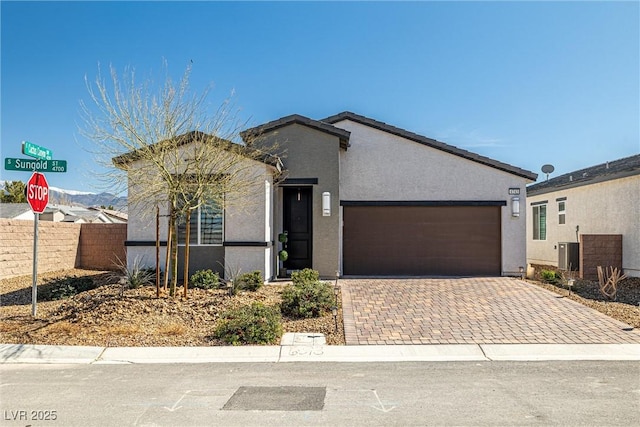 view of front of house with stucco siding, decorative driveway, fence, an attached garage, and central AC unit