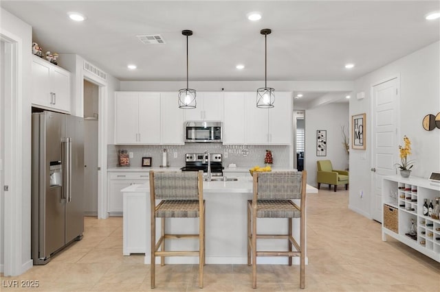 kitchen with a breakfast bar, stainless steel appliances, light countertops, white cabinets, and pendant lighting