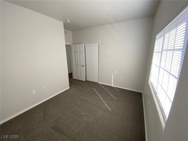 unfurnished bedroom with baseboards, dark colored carpet, and a closet