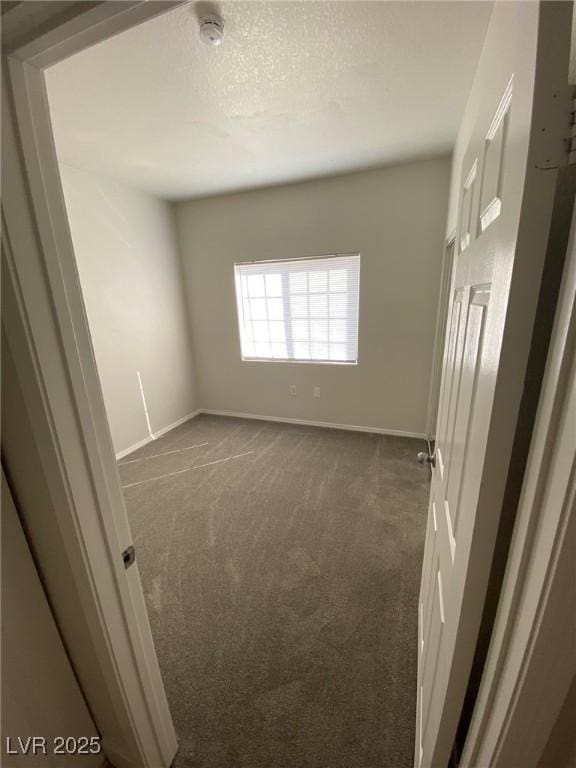 spare room with a textured ceiling, dark carpet, and baseboards