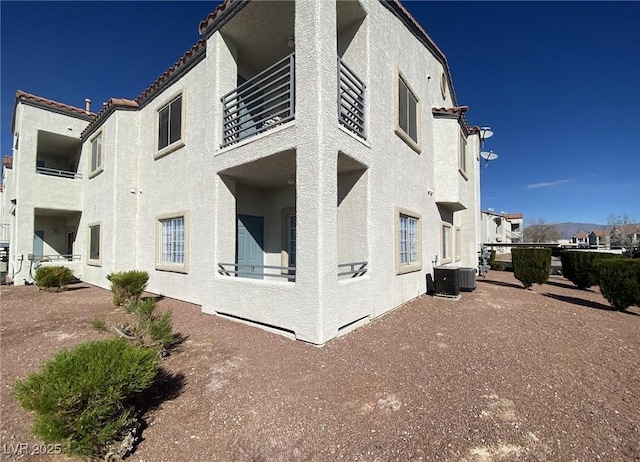 view of side of home featuring a balcony, a tiled roof, cooling unit, and stucco siding