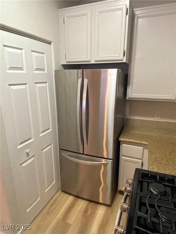 kitchen with light wood-style floors, white cabinetry, range with gas stovetop, and freestanding refrigerator