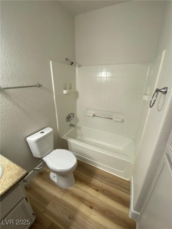 bathroom with a textured wall, toilet, wood finished floors, vanity, and shower / bathing tub combination