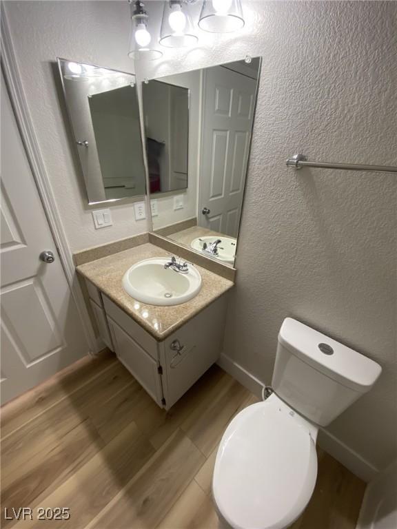 bathroom featuring a textured wall, toilet, vanity, wood finished floors, and baseboards