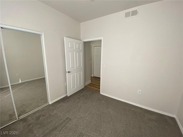 unfurnished bedroom featuring a closet, visible vents, dark carpet, and baseboards