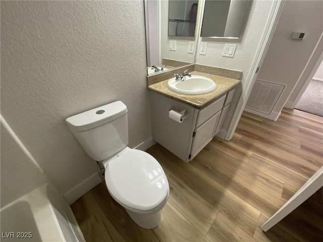 bathroom featuring visible vents, a textured wall, toilet, vanity, and wood finished floors