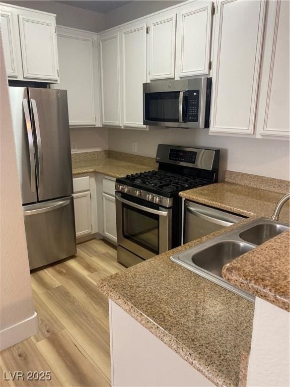 kitchen with white cabinets, light wood finished floors, stainless steel appliances, and a sink