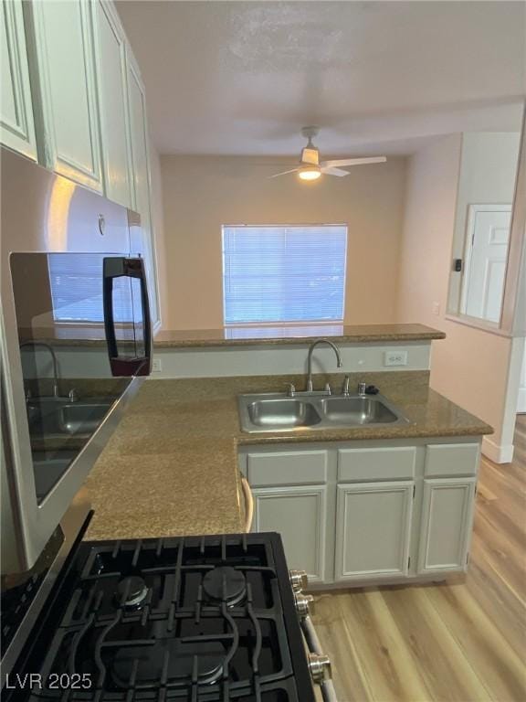 kitchen with ceiling fan, a peninsula, a sink, and light wood-style flooring