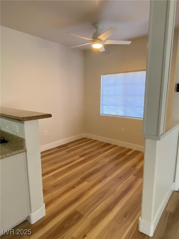 interior space with light wood finished floors, a ceiling fan, and baseboards