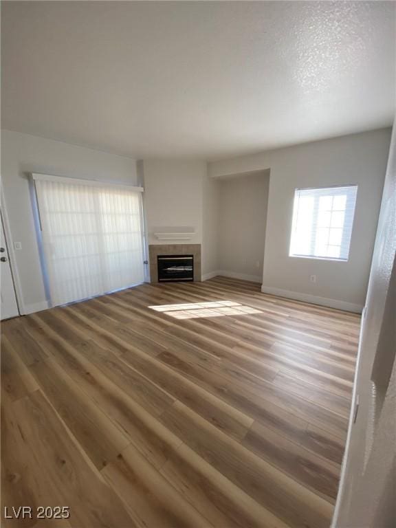 unfurnished living room featuring a fireplace, a textured ceiling, baseboards, and wood finished floors