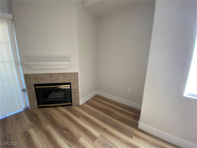 unfurnished living room with a tile fireplace, light wood-style flooring, and baseboards