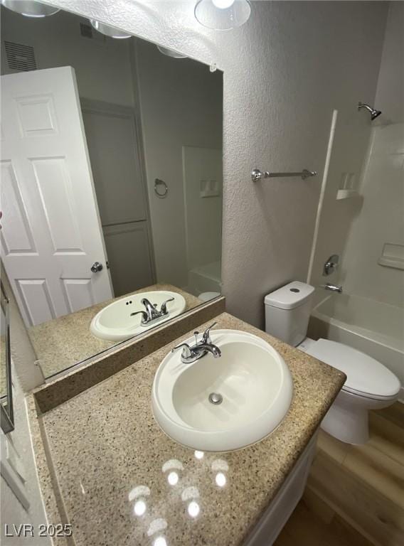 bathroom with shower / washtub combination, a textured wall, toilet, vanity, and wood finished floors