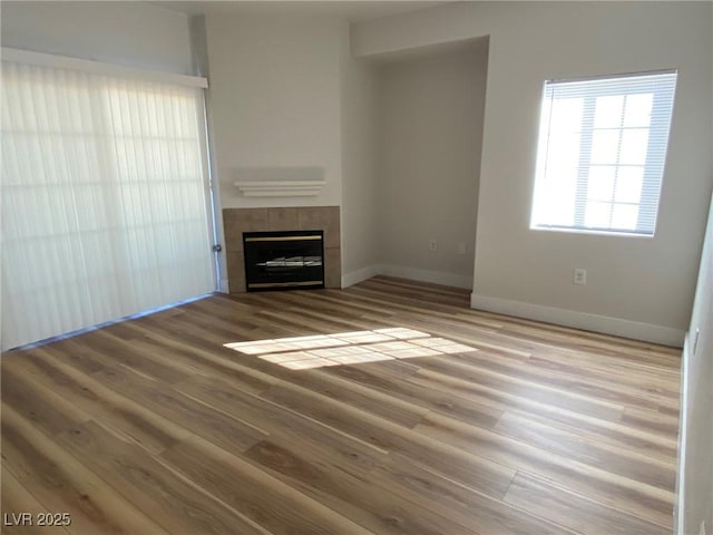 unfurnished living room with wood finished floors, a tile fireplace, and baseboards