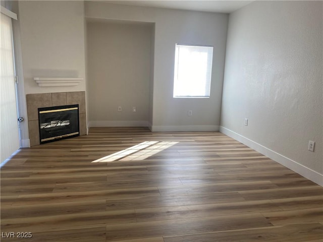 unfurnished living room with wood finished floors, a tile fireplace, and baseboards