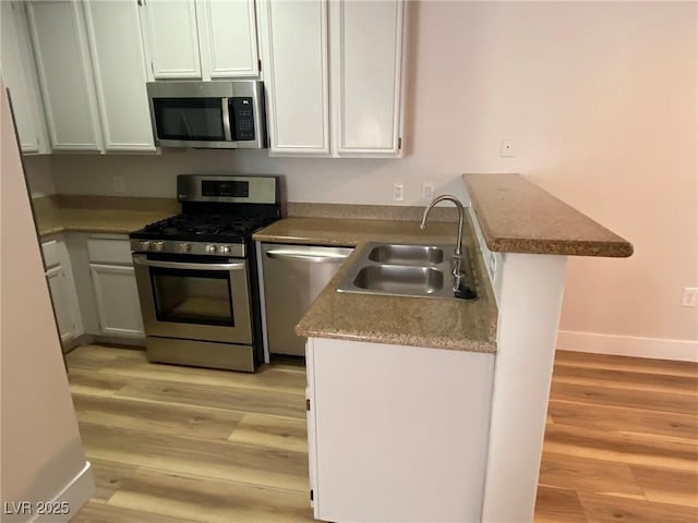 kitchen with a peninsula, light wood finished floors, appliances with stainless steel finishes, and a sink