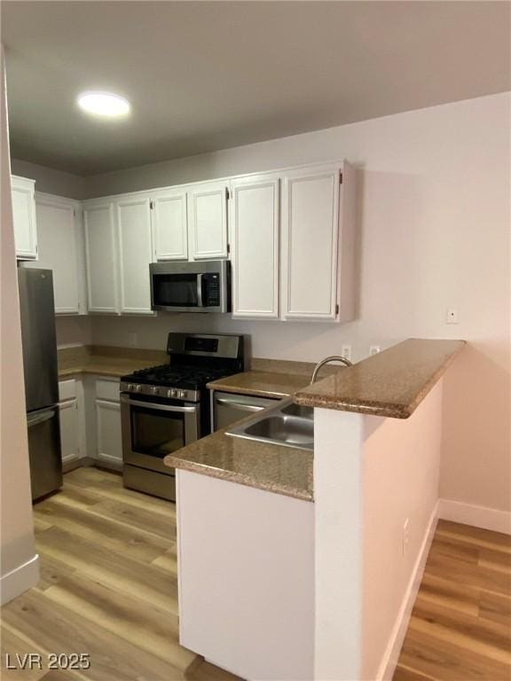 kitchen featuring appliances with stainless steel finishes, white cabinetry, light wood-style flooring, and a peninsula